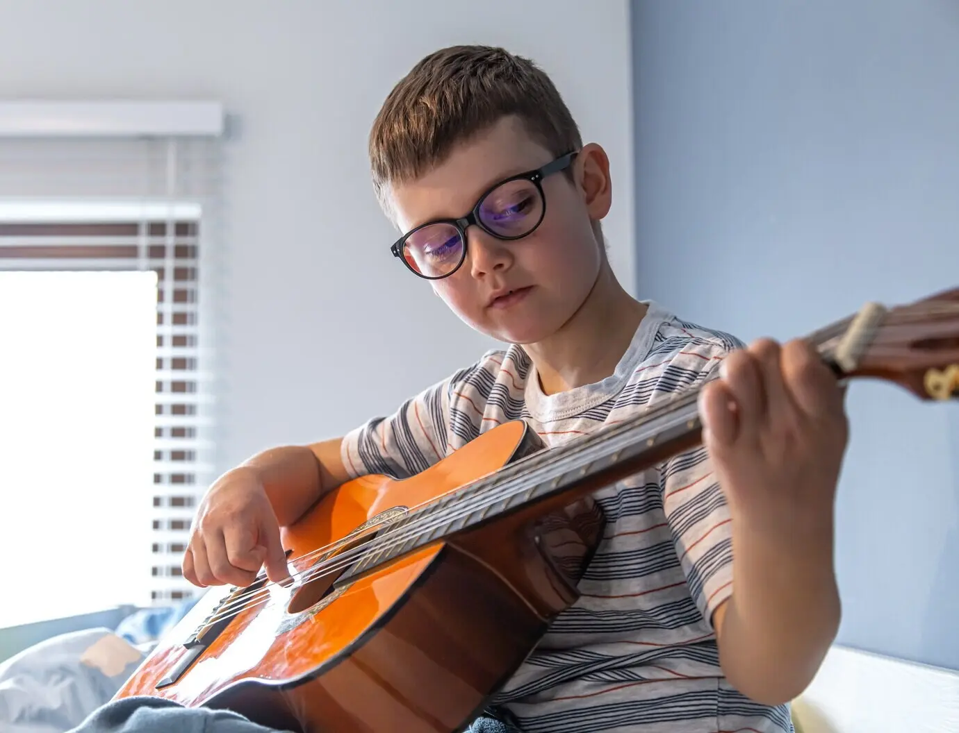 Nahaufnahme eines niedlichen Jungen mit Brille, der zu Hause lernt, klassische Gitarre zu spielen.
